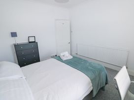 A bedroom with a bed covered in white bedding and a teal throw with towels on top a black dresser with a lamp and a picture frame a white chair and a radiator on the wall at Burry House in Llanmorlais