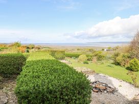 A garden with trimmed hedges and a fire pit overlooking fields and a body of water at Burry House in Llanmorlais