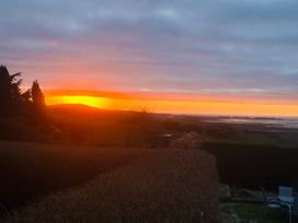 A view of a sunset over the sea with trees and a garden at Burry House in Llanmorlais