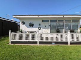 Front view of a white chalet with a fenced deck and outdoor chairs at 56 Cherry Park Chalet in Chapel St Leonards
