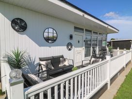 A patio with outdoor seating and cushions next to a white paneled building at 56 Cherry Park Chalet in Chapel St Leonards