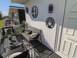 A small outdoor seating area with black chairs, a table with a plant, decorative wall hangings, and a white door at 56 Cherry Park Chalet in Chapel St Leonards