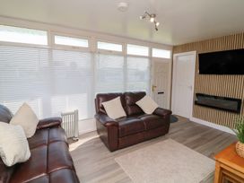 A living room with leather sofas cushions a TV on the wall an electric fireplace and a window with blinds at 56 Cherry Park Chalet in Chapel St Leonards