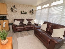 A living room with two brown leather sofas with white cushions and wall shelves with plants at 56 Cherry Park Chalet in Chapel St Leonards