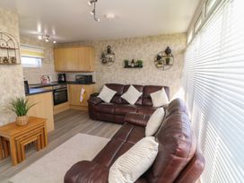 A living room with brown leather sofas next to a kitchen area with wooden cabinets and wall shelves at 56 Cherry Park Chalet in Chapel St Leonards
