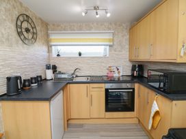A kitchen with wooden cabinets a black countertop a sink oven microwave kettle and wall clock at 56 Cherry Park Chalet in Chapel St Leonards