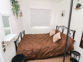 A small bedroom with a black metal bed frame brown bedding two pillows a window with patterned blind and wall shelves with plants at 56 Cherry Park Chalet Chapel St Leonards