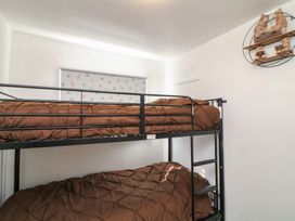 A bedroom with a black metal bunk bed and brown bedding with a window and bird patterned blind at 56 Cherry Park Chalet in Chapel St Leonards