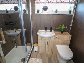A bathroom with a shower enclosure a sink with cabinet a toilet a small trash bin plants and a window at 56 Cherry Park Chalet in Chapel St Leonards