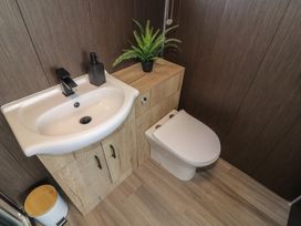 A bathroom with a white sink and toilet with a wooden cabinet and a green plant on top at 56 Cherry Park Chalet in Chapel St Leonards