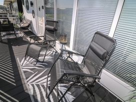A balcony with black reclining chairs and a small table on a patterned rug at 56 Cherry Park Chalet in Chapel St Leonards