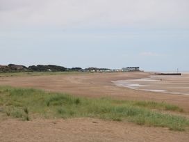 A sandy beach with grassy dunes in the foreground and colorful beach huts in the distance at 56 Cherry Park Chalet in Chapel St Leonards