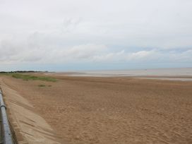 A wide sandy beach with a concrete seawall and railing on the left side at 56 Cherry Park Chalet in Chapel St Leonards