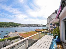 A balcony with a table and blue chairs overlooking a body of water with boats and a hillside town at 5 Esplanade in Fowey