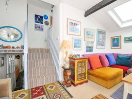 A living room with a yellow sectional sofa with colorful cushions a wooden chest with a table lamp and framed pictures on the walls at 5 Esplanade in Fowey