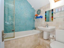 A bathroom with a bathtub tiled in blue and beige a sink a toilet shelves with cups and a mirror at 5 Esplanade in Fowey
