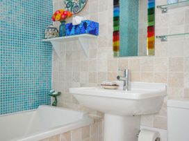A bathroom with a white bathtub and sink blue tiled wall a colorful mirror and a shelf with flowers and a tissue box at 5 Esplanade in Fowey