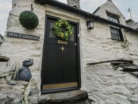 A black door with a wreath and a sign reading PEN-Y-GRISIAU on a white stone wall at Penygrosiau in Barmouth