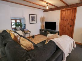 A living room with a black sofa and cushions a TV on a stand a wooden door and a window with a plant at Penyrgrisiau in Barmouth