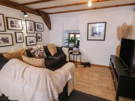 A living room with a black sofa and throw pillows a small side table with plants a black TV stand with a television and framed pictures on the walls at Penyrgrisiau in Barmouth
