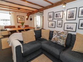 A living room with a dark sectional sofa with cushions a wooden dining table with chairs and hanging lights at Penngrisiau in Barmouth