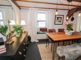 A dining room with a wooden table surrounded by brown chairs a bench with a fur cover a black dresser with books lamps and decorative giraffes white curtains and a window at Penygresiau in Barmouth