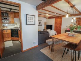 A dining area with a wooden table and chairs and a living room with a sofa and television next to a kitchen with wooden cabinets at Penygrosiau in Barmouth
