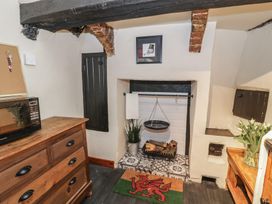 A kitchen corner with a wooden dresser holding a microwave a small fireplace with logs and a hanging pan a doormat with a red dragon and a wooden cabinet with a vase of tulips at Penngrisiau in Barmouth