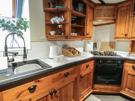 A kitchen with wooden cabinets a black oven a gas stove a white electric kettle two white mugs and a black sink with a faucet at Penyrgrisiau in Barmouth