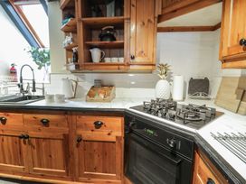 A kitchen with wooden cabinets a gas stove a white kettle and mugs at Penygrisiau in Barmouth