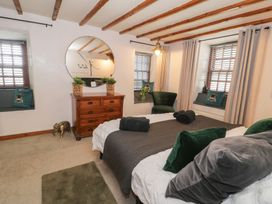 A bedroom with a bed a wooden dresser two windows with curtains and blinds and two green chairs at Penygrisiau in Barmouth