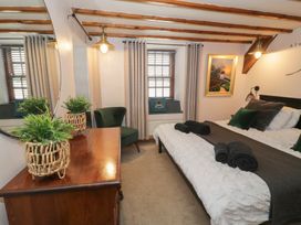 A bedroom with a bed a wooden dresser with plant a green chair and windows with curtains at Penygrisiau in Barmouth