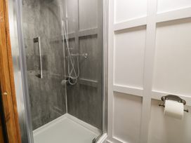 A shower stall with glass door and gray tiles next to a white wall with toilet paper holder at Pen y Grisiau in Barmouth