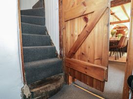 A stairway with dark carpet next to a wooden door opening to a dining area with chairs and flowers at Penygirsiau in Barmouth