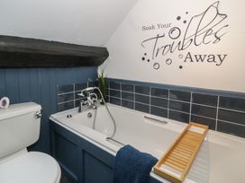 A bathroom with a bathtub a toilet a blue towel and a wooden bath tray with wall text at Penyrgrisiau Barmouth