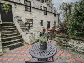 An outdoor patio area with a metal table and chairs a potted plant on the table stone steps leading to a black door and white stone building with multiple windows and flower pots at Penygrisiau in Barmouth