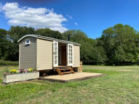 A shepherd hut with open doors in a grassy field with trees and a blue sky at Shepherd Hut 1 Northchapel