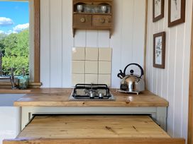 A kitchen counter with a gas stove kettle and dishes on shelves at Shepherd Hut 1 in Northchapel