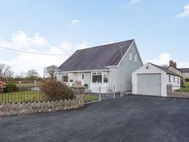 A detached house with a steep roof and an adjacent garage with a paved driveway and a fenced front garden at Bryn Derw in Caernarfon