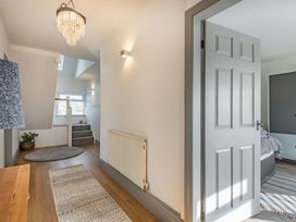 A hallway with wooden floor rugs a grey door and stairs leading up at Bryn Derw in Caernarfon