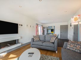 A living room with gray sofas throw pillows a wall-mounted TV electric fireplace and a view into a kitchen and dining area at Bryn Derw in Caernarfon