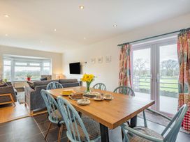 A dining area with a wooden table set with cakes and cups and a living room with sofas and a television at Bryn Derw in Caernarfon