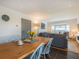 A dining area with a wooden table and blue chairs next to a living room with grey sofas and a bay window at Bryn Derw in Caernarfon