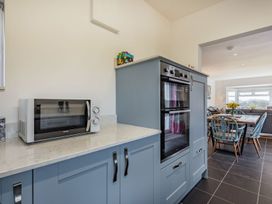 A kitchen with blue cabinets a built-in double oven a microwave on the countertop and a dining area with chairs and a table with flowers at Bryn Derw in Caernarfon