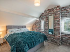 A bedroom with a double bed with teal fur blanket and two pillows beside two small windows with blinds and a wall mirror at Bryn Derw in Caernarfon