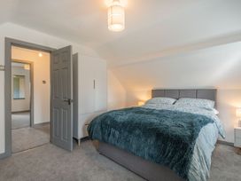 A bedroom with a double bed covered by a dark blanket beside a white wardrobe at Bryn Derw in Caernarfon