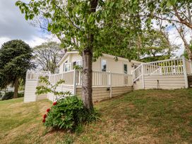 A house with a white fence and open windows on a grassy slope with trees and flowers at 155 Woodland Hall Lyons in Ruthin