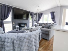 A living room with grey sofas cushions a wall-mounted television and windows with curtains at 155 Woodland Hall Lyons in Ruthin