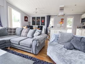 A living area with grey sofas pillows a kitchen island with flowers and a dining table with chairs at 155 Woodland Hall Lyons Ruthin