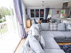 A living room with a large grey sectional sofa and a dining table with chairs next to a kitchen area with bar stools and a countertop at 155 Woodland Hall Lyons in Ruthin